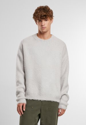 Pullover grigio chiaro, morbido, con collo rotondo e orlo a coste, dotato di maniche lunghe e vestibilità ampia. Indossato su pantaloni verde oliva.