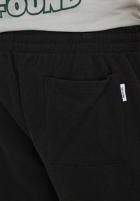 Gros plan sur un pantalon à taille élastique noire avec une poche arrière ornée d'une petite étiquette blanche "ONLY & SONS".
