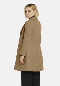 Lange beige jas met een gestructureerd ontwerp, twee knopen en een reverskraag. Gemaakt van textiel met textuur, gezien vanuit de achterkant.