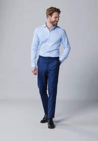 Lichtblauw, lang overhemd met knopen, gecombineerd met op maat gemaakte donkerblauwe broeken en zwarte nette schoenen, met een slanke pasvorm en gladde texturen.