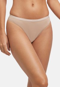 Beige Tanga-Unterwäsche mit glatter Textur, gebrandeter Bund mit der Aufschrift "FALKE" und niedrig sitzendem Schnitt für Komfort und Passform.