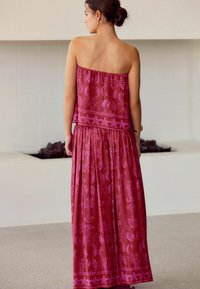 Mouwloze, vloeiende maxi-jurk van dieproze stof met een herhaald schelp- en sterrenpatroon. Elastische taille met een geraffineerde textuur aan de onderkant.