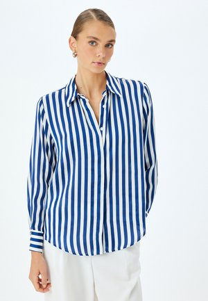 Camisa a rayas en azul y blanco, hecha de tela suave, con un frente abotonado, cuello clásico y mangas largas con puños abotonados.