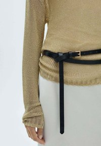 Pull en maille or clair à manches longues légèrement resserrées au poignet et ceinture en cuir noire nouée autour de la taille, avec un bout lâche qui pend.