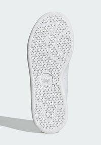 White rubber sneaker sole with distinctive tread pattern, featuring circular textures and a prominent Adidas logo at the heel.