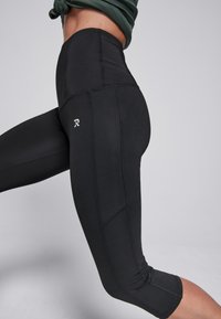 Zwarte sportleggingen met een hoge taille, strakke pasvorm en een textuurpatroon op de stof, met een logo op de dij.