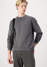Gray sweatshirt in a soft, textured fabric with ribbed cuffs and hem. Paired with dark jeans and a black crossbody bag.