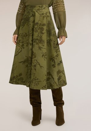 Midi-rok met hoge taille in olijfgroen met bloemenprint, gecombineerd met een bijpassende geborduurde blouse met lange mouwen en donkerbruine suède laarzen tot aan de knie.