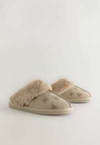 Chaussons beiges avec un revers en fausse fourrure beige moelleux, présentant un motif animalier doré discret sur un tissu doux, et une semelle profilée basse.