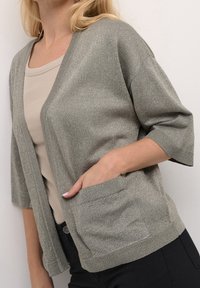 Glanzend grijze cardigan met korte mouwen, open voorkant en voorzakken. Zachte textuur met een subtiele metalen draad.
