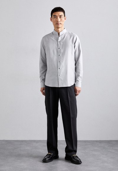 Camisa botón gris claro con cuello alzado, combinada con pantalones de pierna ancha negros y mocasines negros con detalles en oro.
