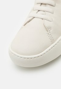 Sneaker in pelle bianca con texture liscia, punta arrotondata, cuciture a contrasto e lacci piatti. Design semplice senza branding visibile.