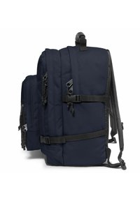 Tmavě modrý batoh s aerodynamickým designem, který má více přihrádek, černé zipy, texturované popruhy a nastavitelné spony.