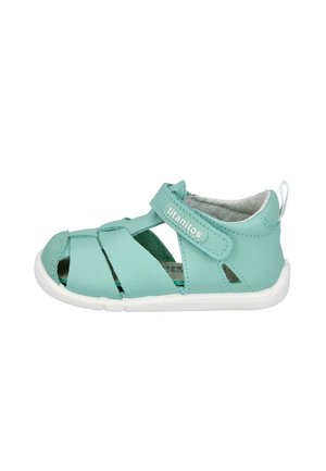 Sandalia turquesa con diseño de punta cerrada, hecha de cuero suave, con una correa de Velcro y suela de goma blanca para mayor comodidad y agarre.