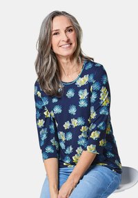 Marinebluse mit drei Viertelärmeln; mit leuchtend gelben und blauen Blumenmustern; aus weichem Stoff, runder Ausschnitt und lockere Passform.