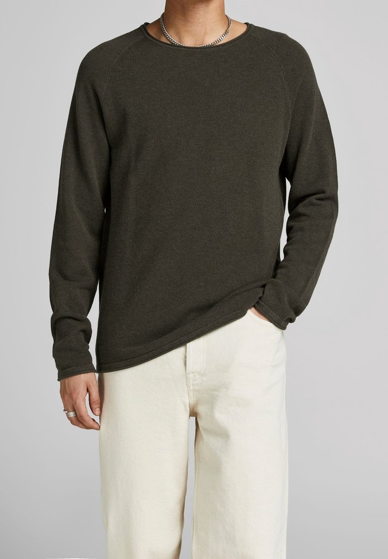 Pull en tricot texturé vert foncé à manches longues et col rond, associé à un pantalon écru. Présente une coupe décontractée et des accents côtelés subtils.
