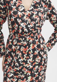 Robe à manches longues avec un décolleté en V profond, présentant un fond noir et un motif floral abstrait multicolore en rouge, vert et beige.