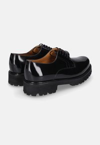 Een paar glanzende zwarte leren derby schoenen met dikke profielzolen en zwarte veters, weergegeven van de achterkant op een witte achtergrond.