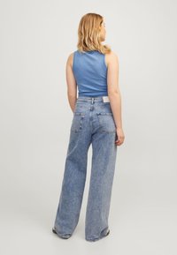 Top de alças azul com textura, combinado com jeans claros de cintura alta e pernas largas, apresentando bolsos traseiros e um discreto rótulo na cintura.