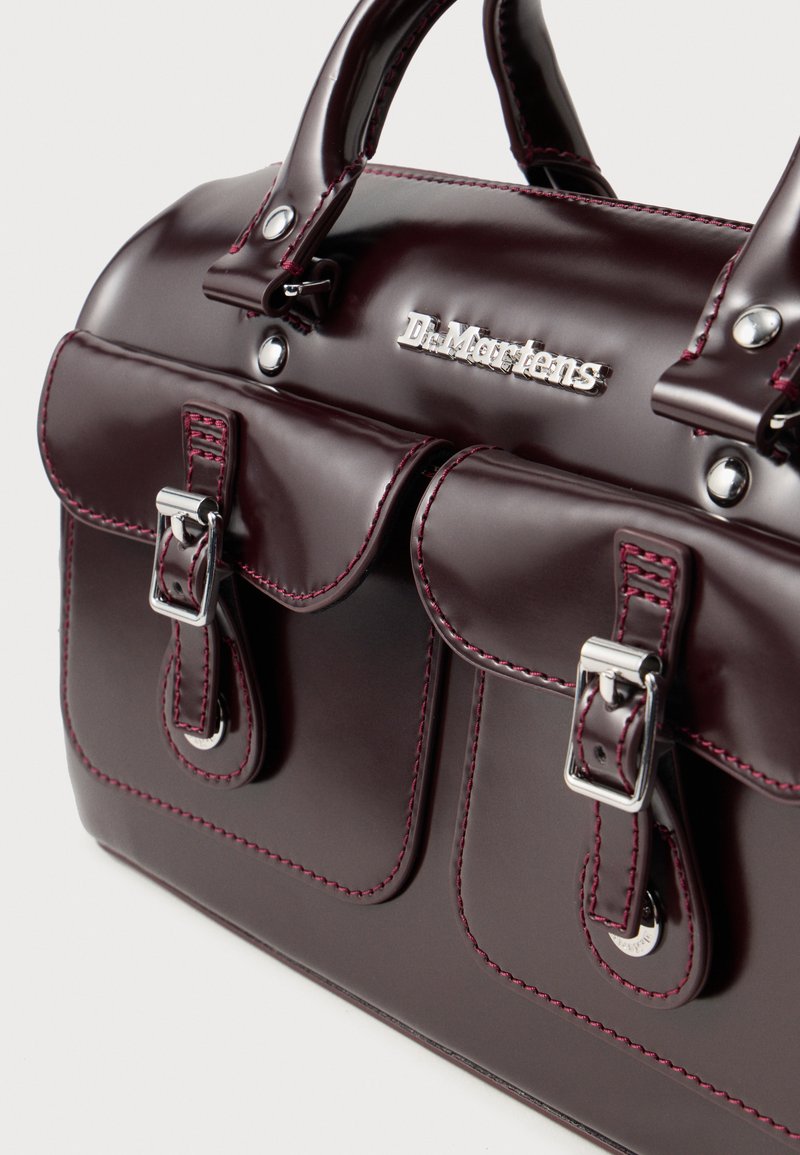 Borsa a mano in ecopelle borgogna con doppi taschini frontali, accessori in argento e cuciture rosa a contrasto. Presenta manici arrotondati e logo del marchio.