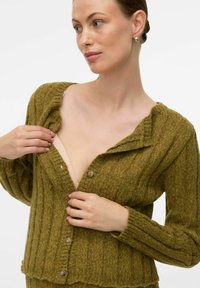 Olivgrön ribbad cardigan med knäppning, med veckad krage och texturerad stickad tyg. Sitter åtsittande vid midjan.