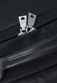 Black nylon bag featuring silver zippers with heart-shaped pullers and a textured surface. Includes a smooth leather handle for grip.