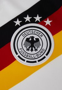 Blason avec un aigle noir et le texte "Deutscher Fussball-Bund" accompagné de quatre étoiles au-dessus, sur un fond en tissu aux rayures noires, rouges et jaunes.