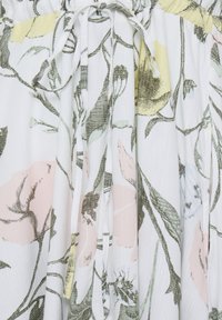 Tissu blanc avec un motif floral pastel doux en rose, jaune et vert, avec une ceinture froncée et un cordon de serrage noué.