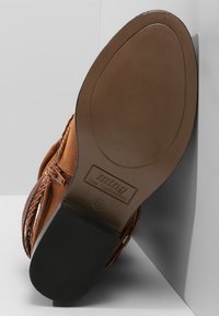 Stivale in suede marrone con dettagli intrecciati, punta rotonda e suola in gomma liscia. Presenta il logo e la taglia impresso sul tallone.