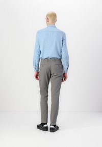 Chemise en denim bleu clair à manches longues, associée à un pantalon gris slim et des baskets noires. Design simple, sans motifs ni logos visibles.