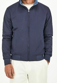 Veste bomber bleu marine avec une fermeture éclair à l'avant, des poignets et un ourlet côtelés, une texture douce et un col intérieur bleu clair.
