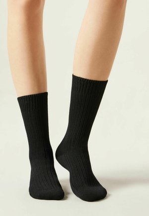 Schwarze gerippte Socken mit einer weichen Textur, ausgestattet mit einem bequemen Bündchen oben und einer figurbetonten Form, designed für den täglichen Gebrauch.
