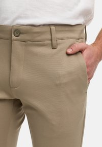 Pantalones beige de tela suave con corte recto, cierre de un botón y bolsillos laterales, que presentan un sutil patrón texturizado.