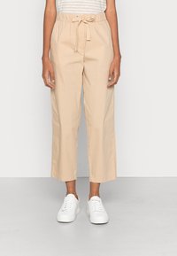 Pantaloni beige a vita alta con coulisse, caratterizzati da una texture liscia e una vestibilità comoda, abbinati a sneakers bianche.