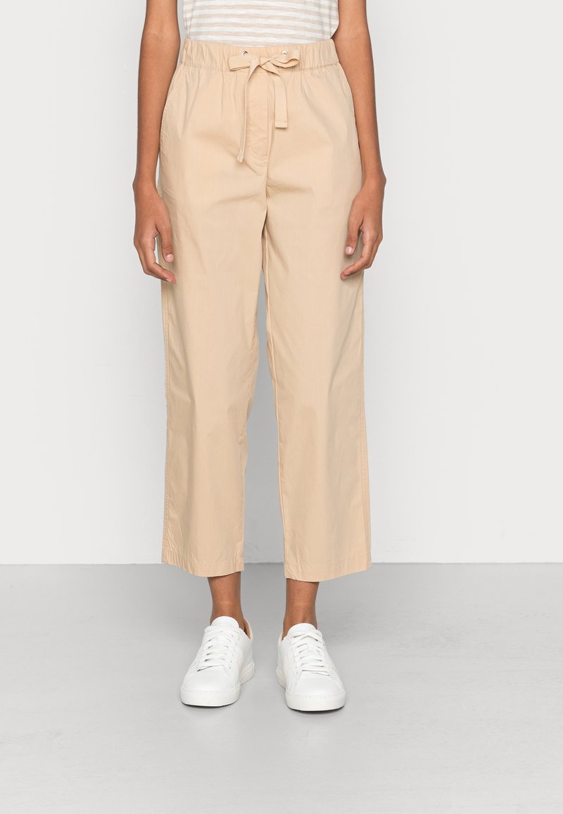 Pantaloni beige a vita alta con coulisse, caratterizzati da una texture liscia e una vestibilità comoda, abbinati a sneakers bianche.