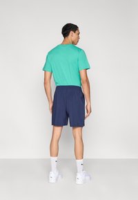 Τυρκουάζ μπλούζα, σκούρο μπλε σορτς, λευκά πάνινα παπούτσια με λογότυπο και λευκές κάλτσες. Λείο ύφασμα, άνετη εφαρμογή και ελαστική ζώνη στη μέση των σορτς.