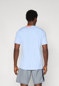 Light blue athletic t-shirt with a round neck, short sleeves, and an orange accent on the back. Soft texture, paired with gray shorts.