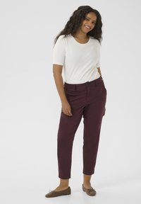 Burgundy trousers with a straight fit, side pockets, and a button closure. Paired with a fitted white short-sleeve top and brown shoes.