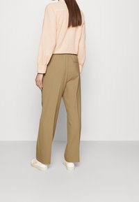 Tan wijde broek met een ontspannen pasvorm, voorzien van een elastische tailleband. Gepaard met een licht perzikkleurig blouse met stippen en witte sneakers.