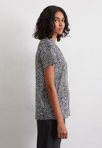 Short-sleeve black and white patterned top with a relaxed fit, round neckline, and a slightly longer back hem. Soft fabric texture.