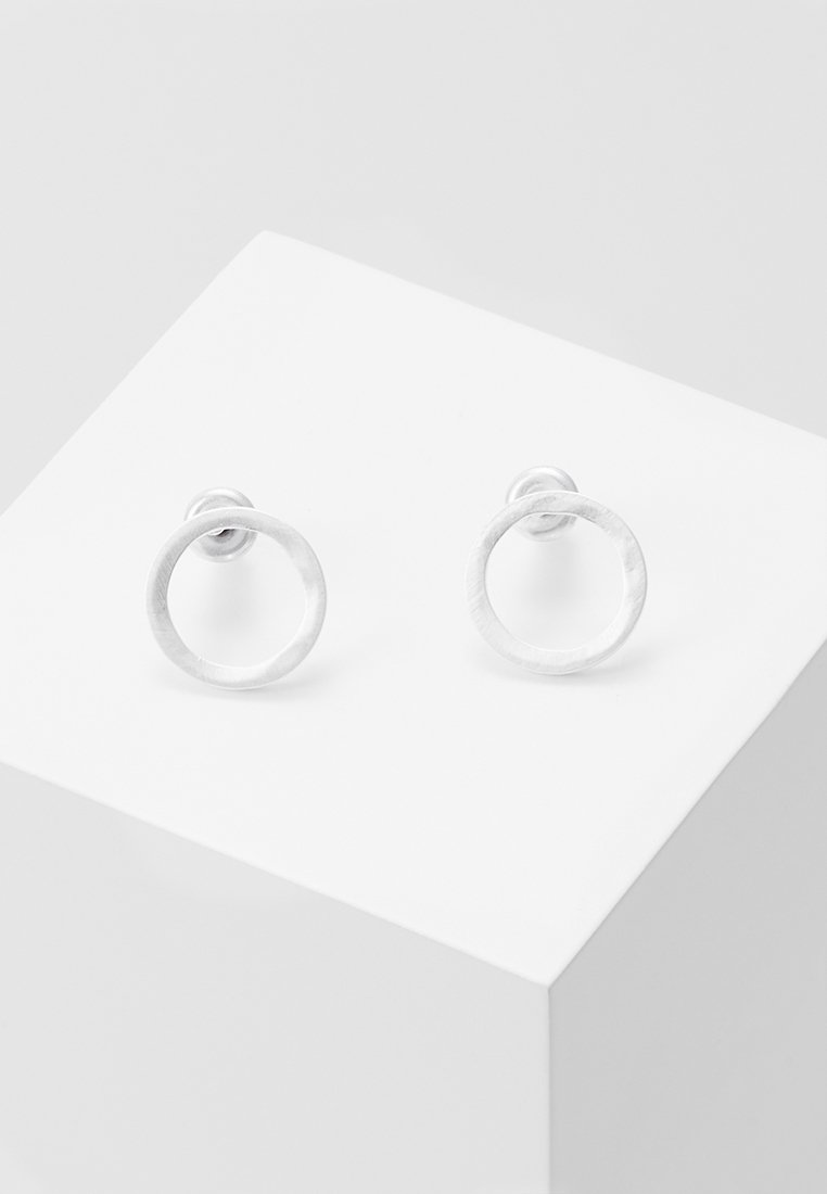 Paire de petites boucles d’oreilles clous rondes en argent avec une texture martelée, posées sur un socle blanc en forme de cube.