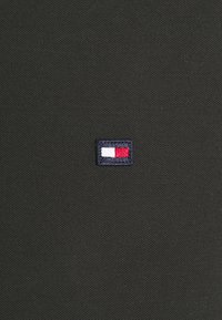 Svart texturerad tyg har en liten, rektangulär broderad logotyp med blå, vit och röd som är centrerad på den.