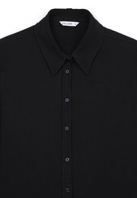 Maglia nera a maniche lunghe con colletto a punta, sei bottoni neri nella parte anteriore e un piccolo etichetta bianca all'interno del colletto.