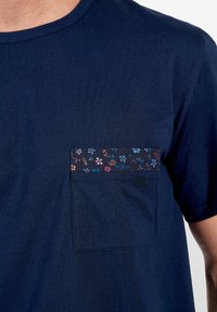 Marinblå kortärmad T-shirt med ficka med blommönster som accent. Mjuk bomullstyg, rund hals och en diskret logotyp på fickan.