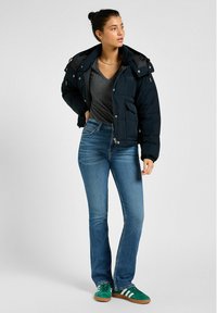 Mörkblå jacka i puffmodell med dragkedja fram, två fickor och elastiska ärmslut; grå t-shirt med V-hals; blå utsvängda jeans; gröna sneakers med vita ränder.