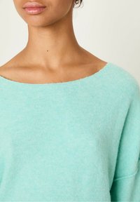 Lys teal sweater lavet af blødt strikket stof, med en bred halsudskæring og en afslappet pasform. Synlig tekstur og foldet manchet detail.