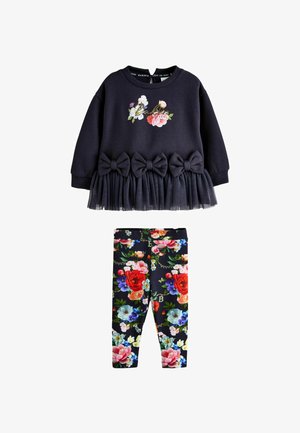 Tumši zils garām piedurknēm tops ar ziedu rakstu, trim lentītēm un tilla apmali, salikts kopā ar tumši zilām legingiem, kas klāti ar daudzkrāsainiem ziedu rakstiem.