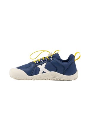 Zapatilla deportiva azul marino con puntera blanca, suela blanca, cordones amarillos, una X blanca en el lateral y lengüetas amarillas en el talón y la lengüeta.