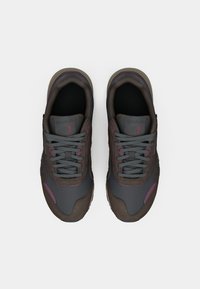 Um par de ténis atléticos em cinza escuro e castanho com atacadores cinzentos, vistos de cima sobre um fundo branco.