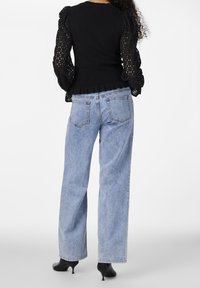 Musta tiukka paita, jossa on kuvioitu, puffatut pitsihihat; yhdistettynä vaaleansinisiin leveisiin farkkuihin ja mustiin kärkitossuihin.